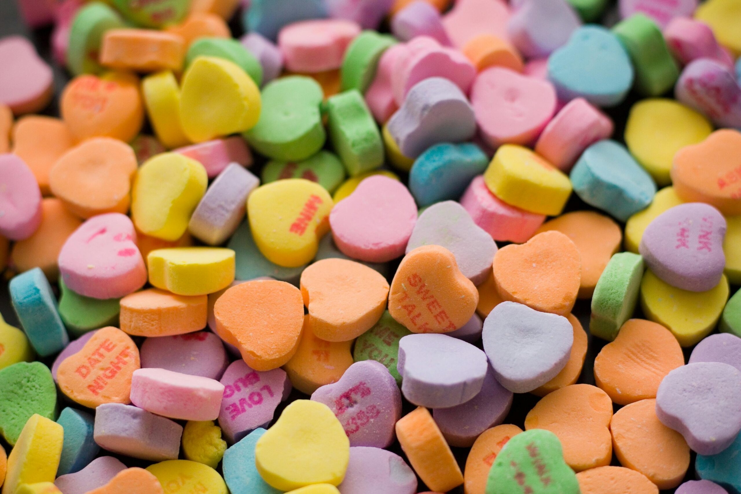 A vibrant collection of colorful, heart-shaped candies with printed phrases.