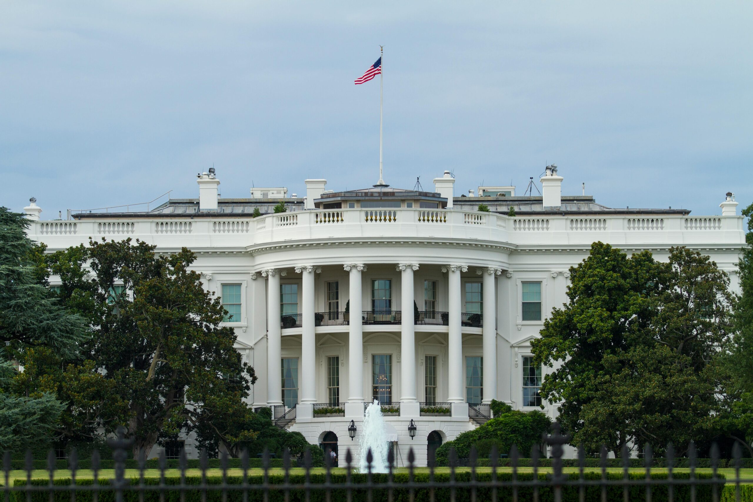 Front view of the iconic White House with the American flag, surrounded by greenery.